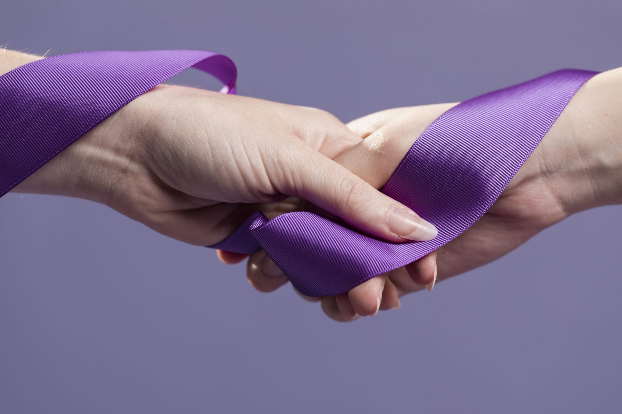 Interlocked hands of two womens, bound by purple suffragette ribbon